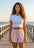 Woman standing on a wooden boardwalk by the ocean wearing a white crop top and pink shorts.