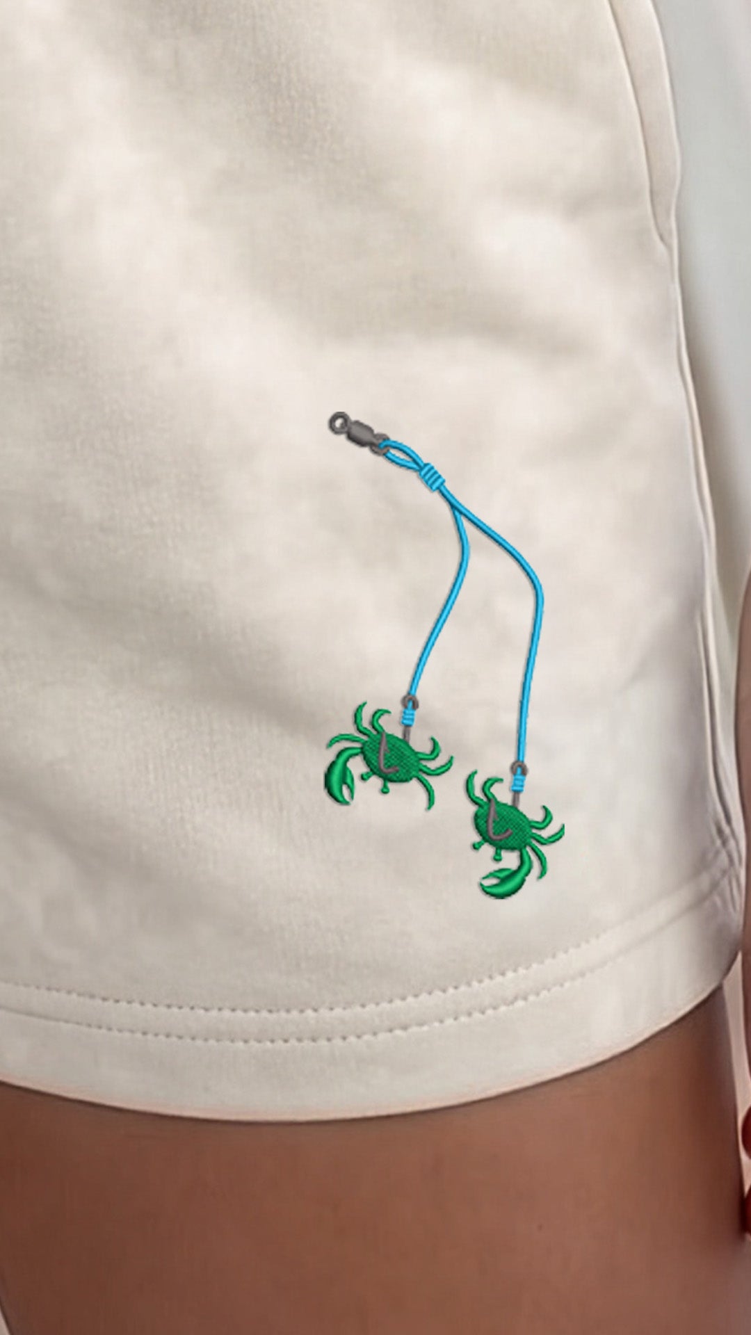 Green crab charms on a blue string attached to a white garment.
