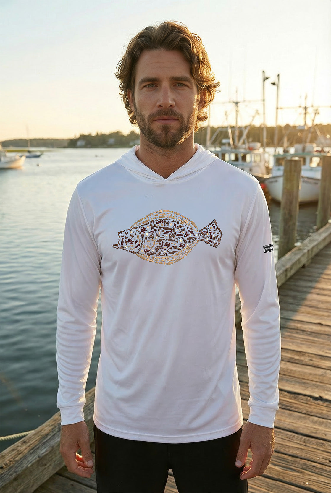 Man wearing a white long-sleeve shirt with a fish design on a dock by a body of water.