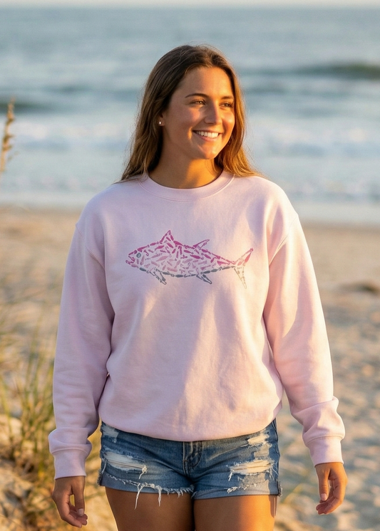 Woman walking on a sandy beach wearing a light pink sweatshirt with a graphic design.