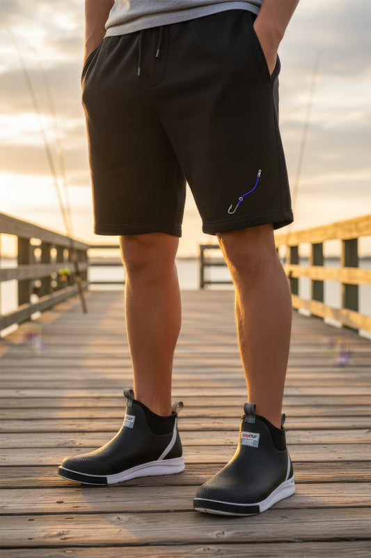 Person wearing black shorts with a blue design and black Chelsea boots on a wooden dock.