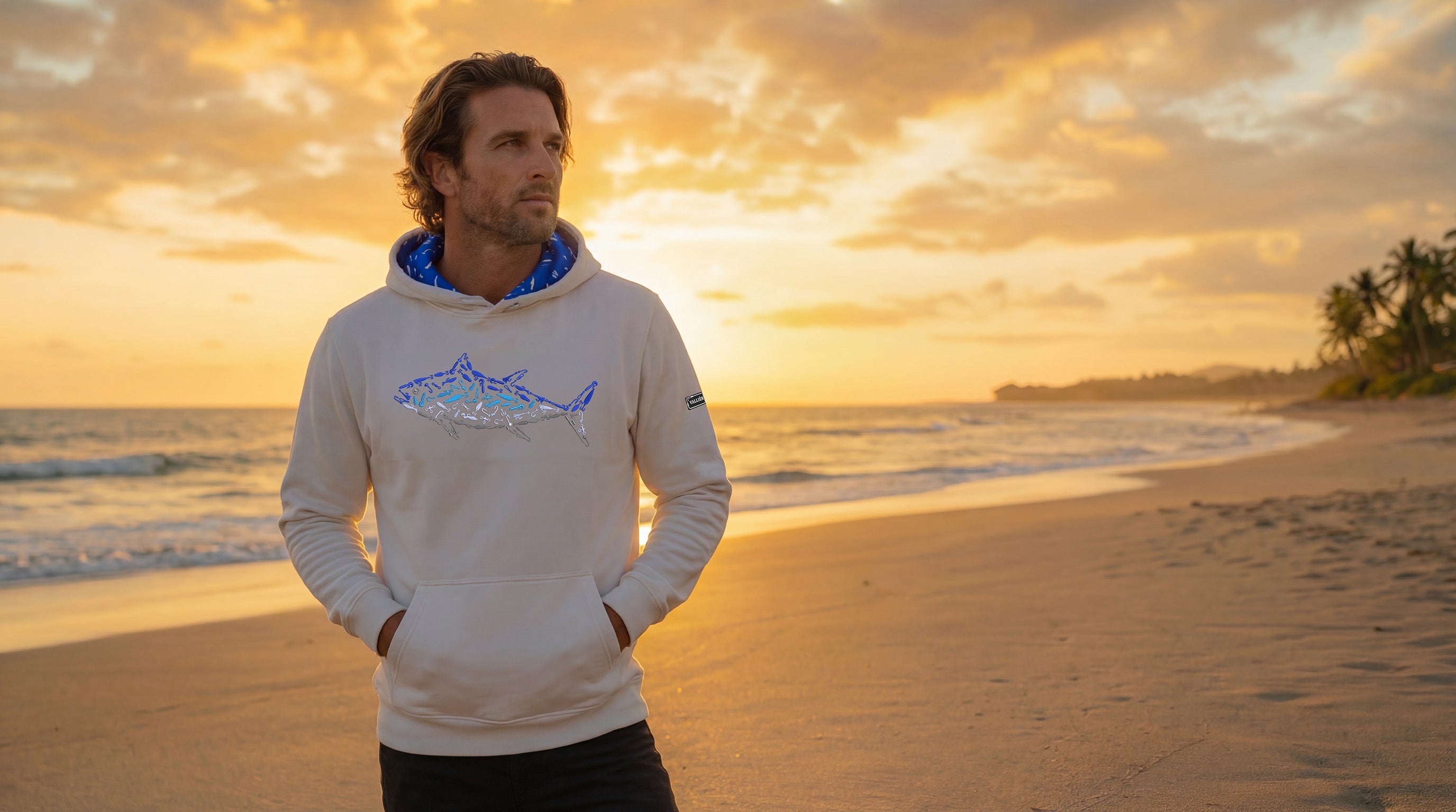 Man wearing a hoodie with a shark design on a beach at sunset