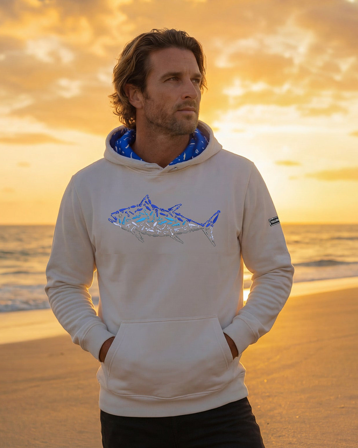 Man wearing a hoodie with a shark design on a beach at sunset