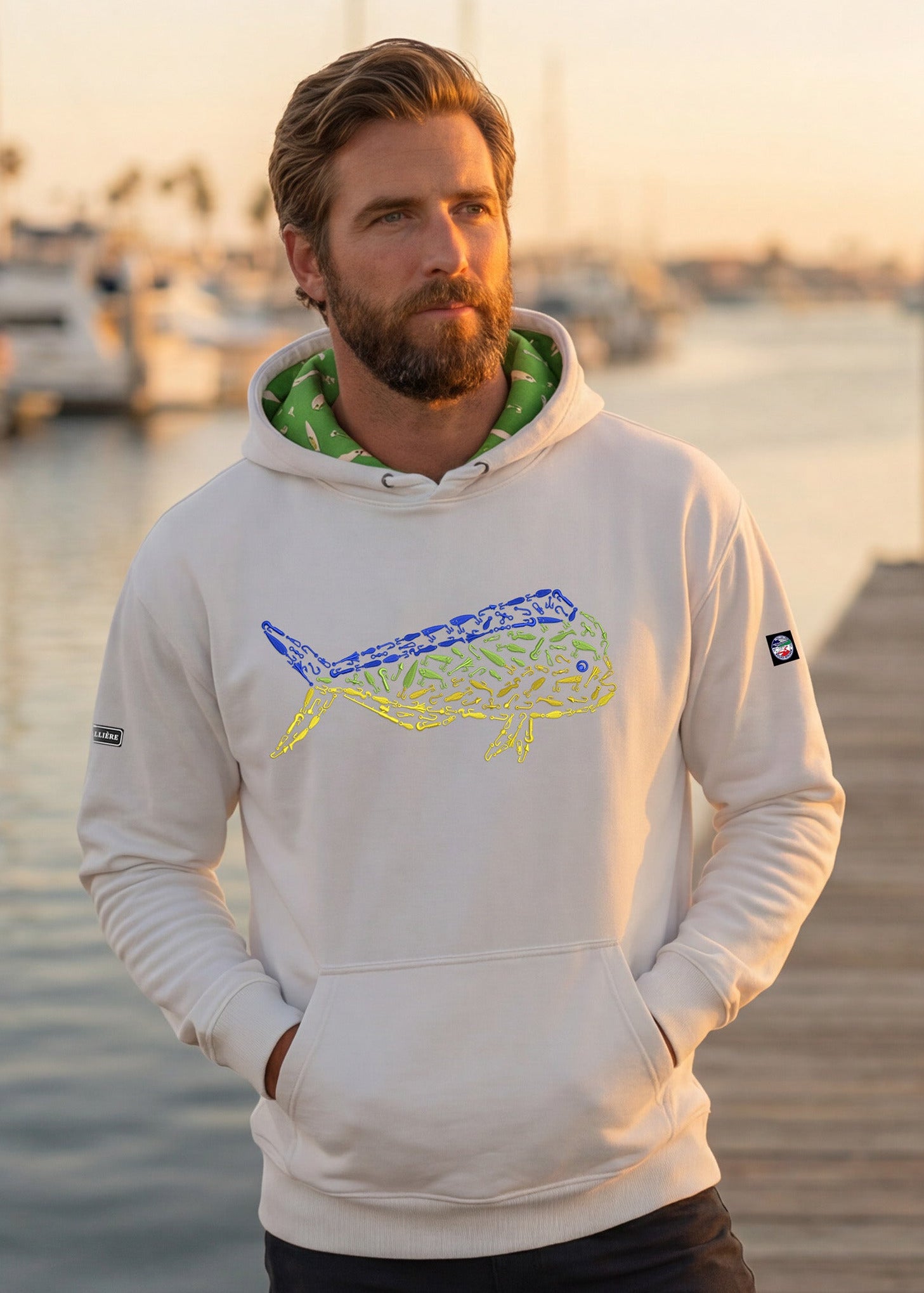 Man wearing a hoodie with a logo on a dock with boats in the background