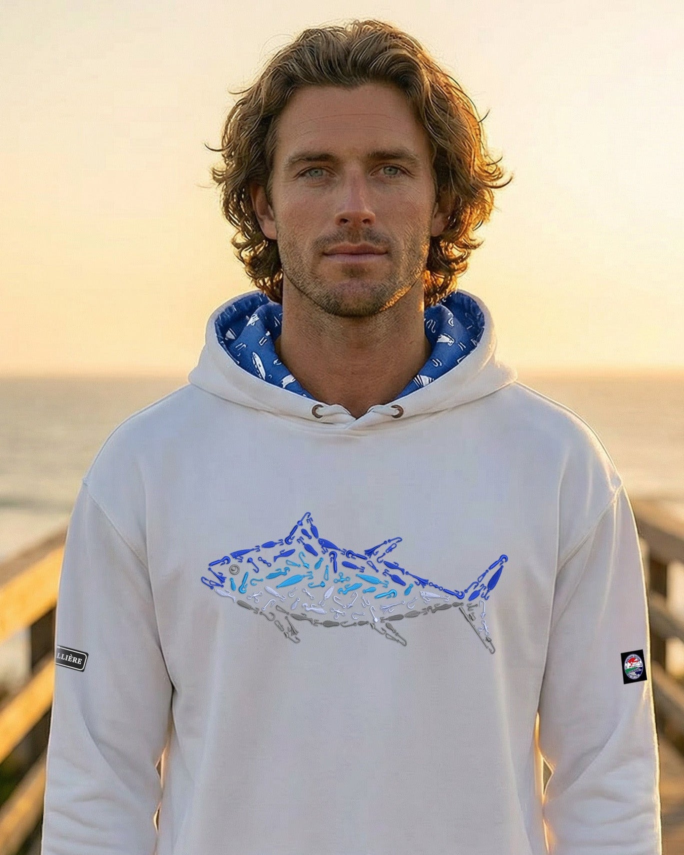 Man wearing a hoodie with a shark design on a wooden pier by the ocean.