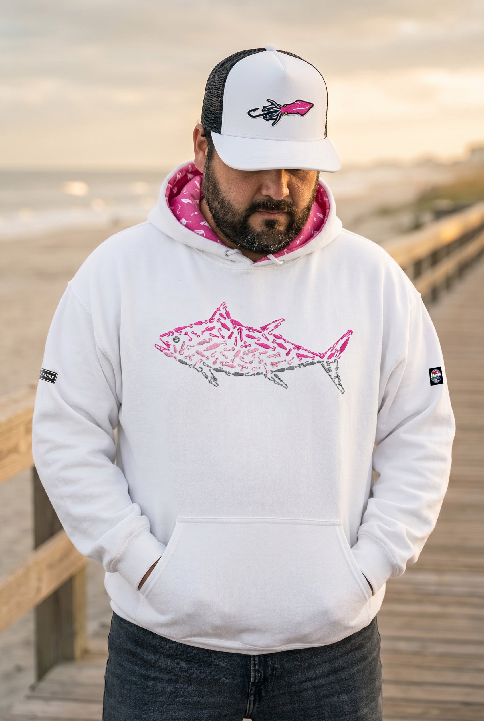 Man wearing a white hoodie with pink and black fish design on a wooden dock.