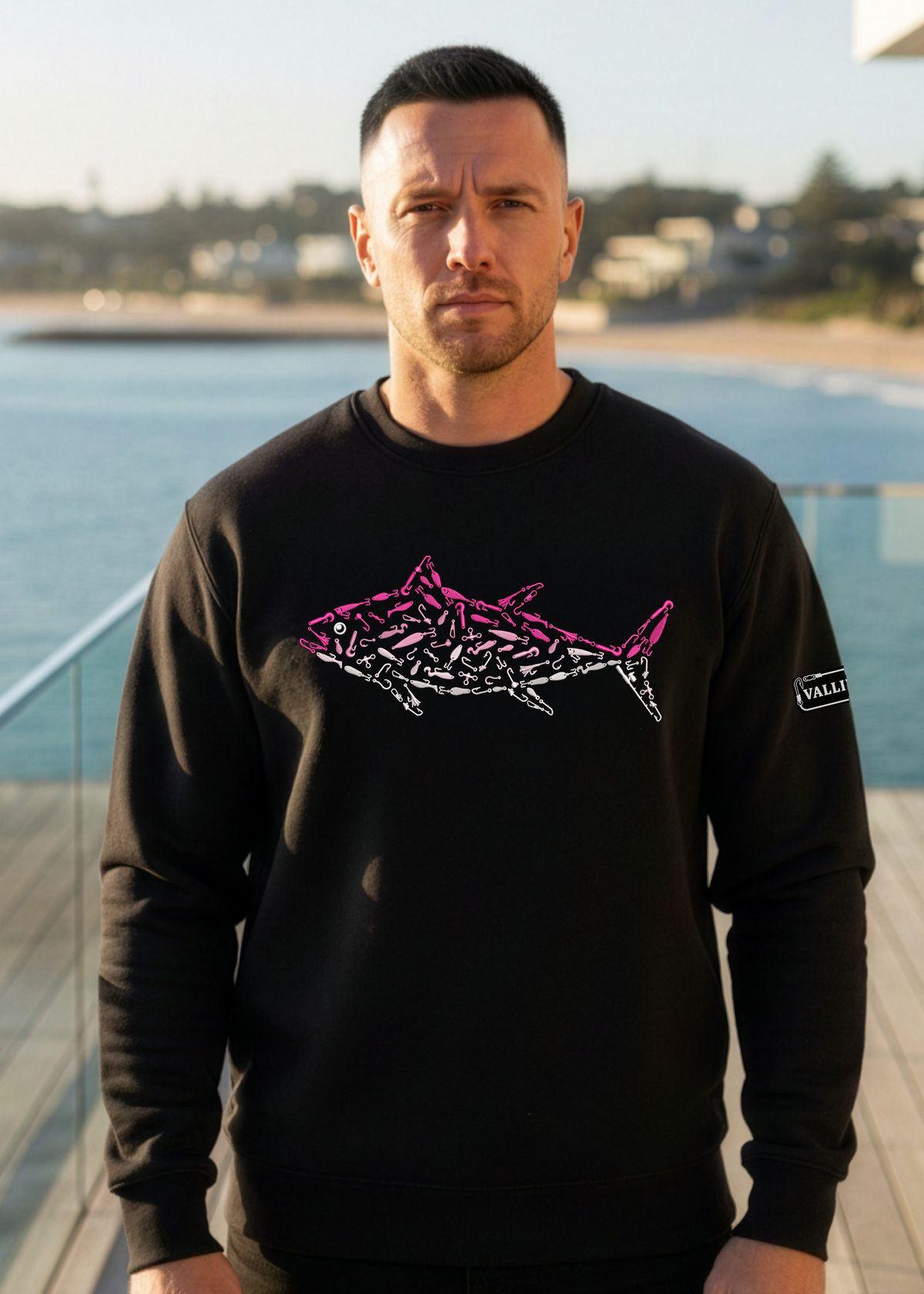 Man wearing a black sweatshirt with a Pink Tuna design by the ocean