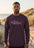 Man wearing a purple long-sleeve shirt with a shark design on a beach