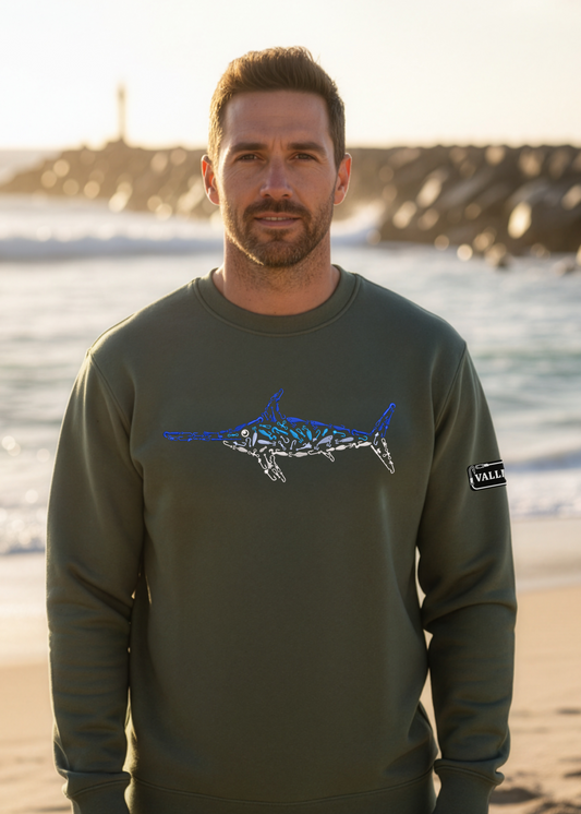 Man standing on a beach wearing a green sweatshirt with a graphic design.