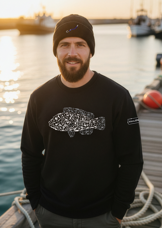 Man wearing a black sweatshirt with a fish design on a dock by water