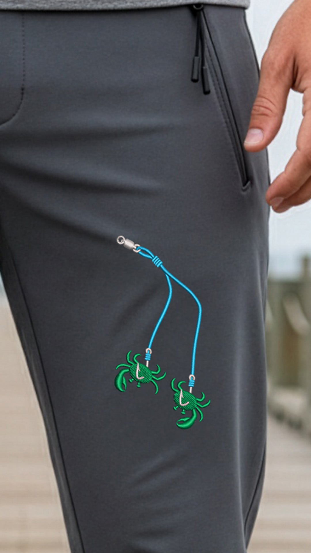 Gray pants with green crab designs and blue strings on a blurred outdoor background